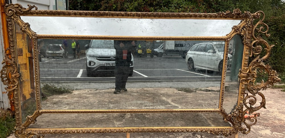 A large nineteenth-century French giltwood border mirror featuring a elaborate rococo crested top, egg and dart moulding, and marginal glass panels. View VII