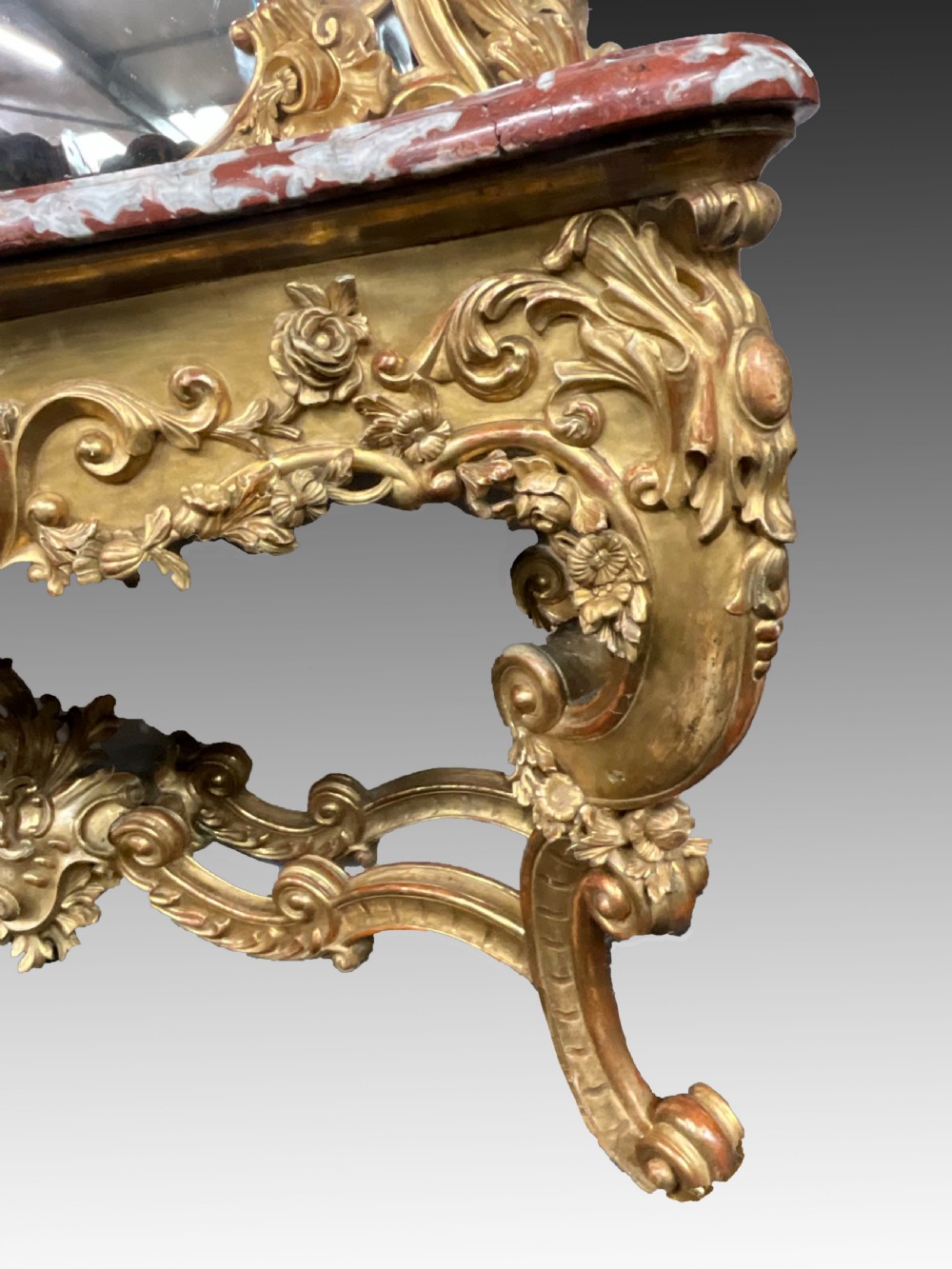 An ornate French Rococo giltwood console table featuring a shaped red marble top and a matching carved mirror frame with foliage cresting. View II