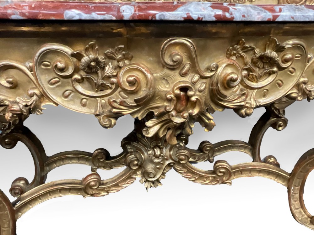 An ornate French Rococo giltwood console table featuring a shaped red marble top and a matching carved mirror frame with foliage cresting. View III