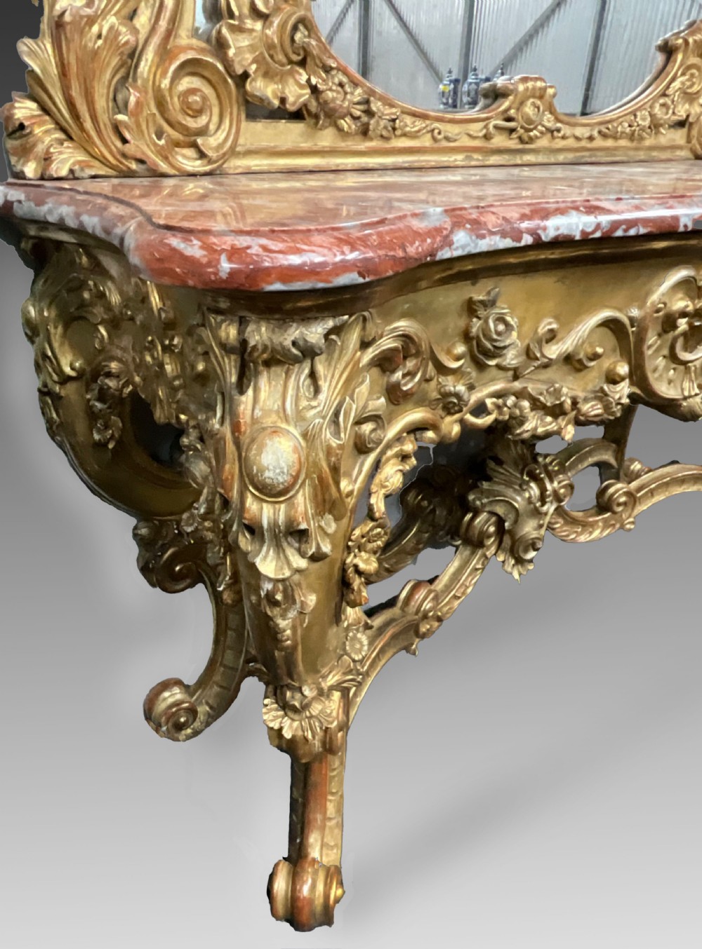 An ornate French Rococo giltwood console table featuring a shaped red marble top and a matching carved mirror frame with foliage cresting. View V