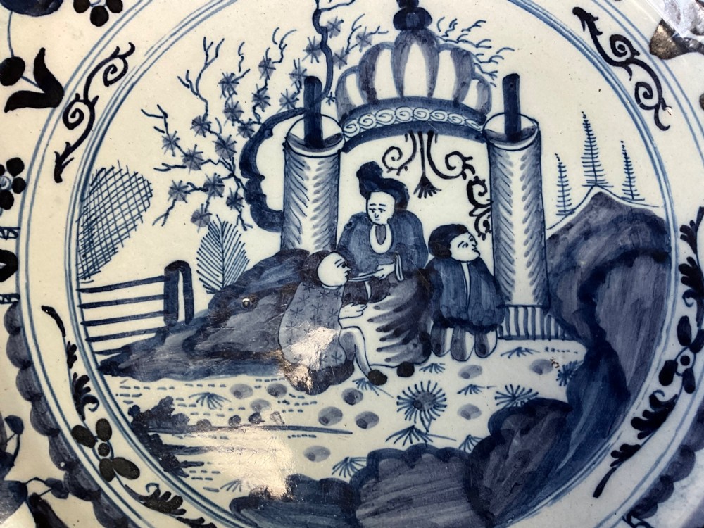 An 18th-century circular Delftware plate featuring hand-painted cobalt blue chinoiserie figures and floral panelled borders on a tin-glazed background. View V