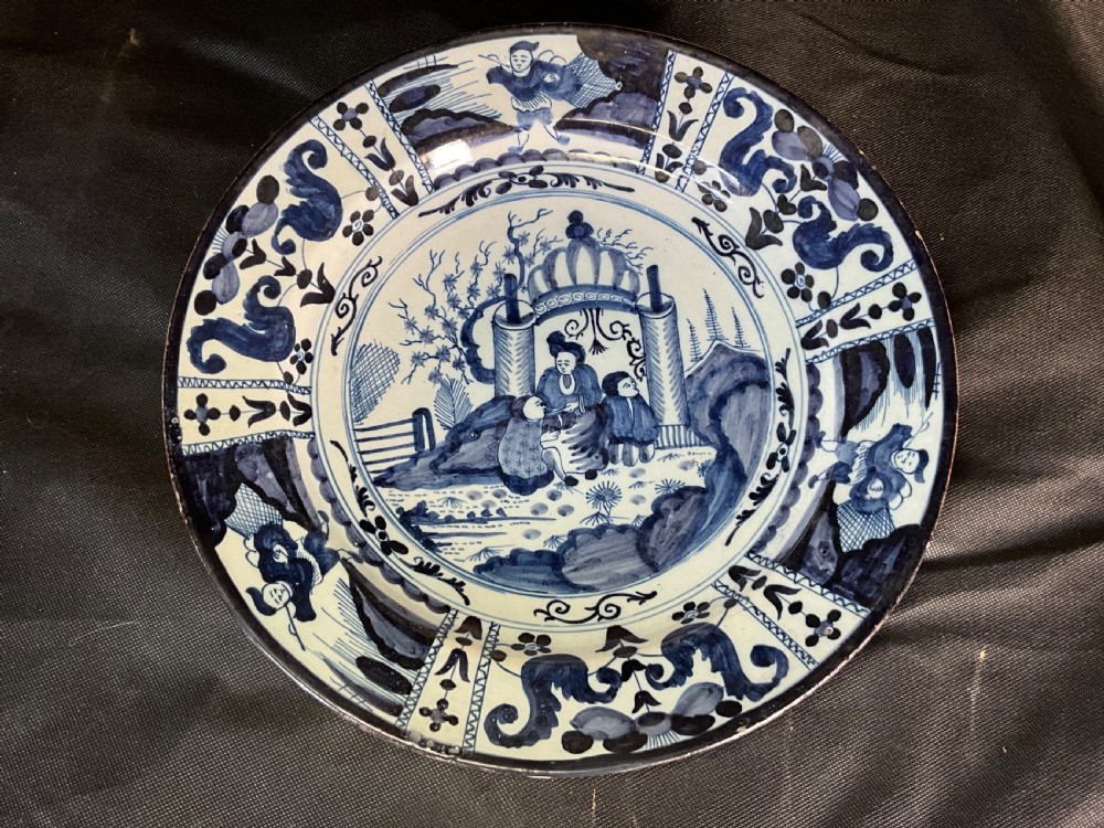 An 18th-century circular Delftware plate featuring hand-painted cobalt blue chinoiserie figures and floral panelled borders on a tin-glazed background. View VI