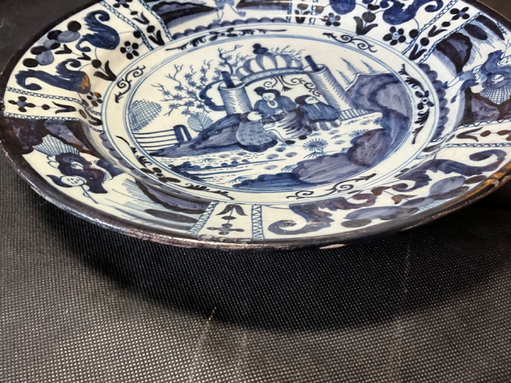 An 18th-century circular Delftware plate featuring hand-painted cobalt blue chinoiserie figures and floral panelled borders on a tin-glazed background. View VIII