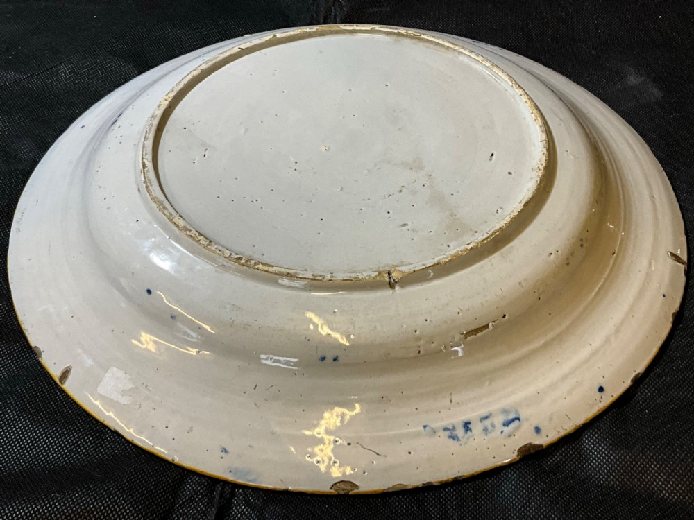 An antique circular tin-glazed earthenware plate featuring hand-painted cobalt blue floral motifs on a white background with a yellow rim. View II