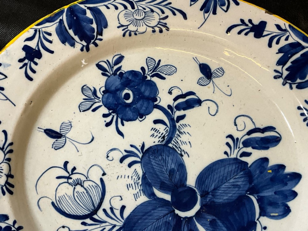 An antique circular tin-glazed earthenware plate featuring hand-painted cobalt blue floral motifs on a white background with a yellow rim. View IV