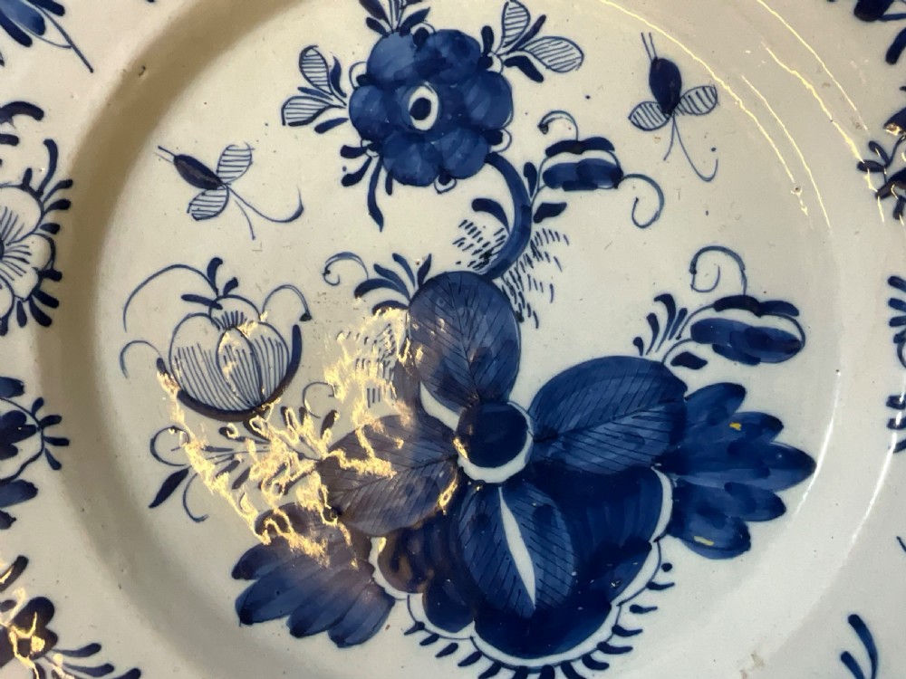 An antique circular tin-glazed earthenware plate featuring hand-painted cobalt blue floral motifs on a white background with a yellow rim. View VI
