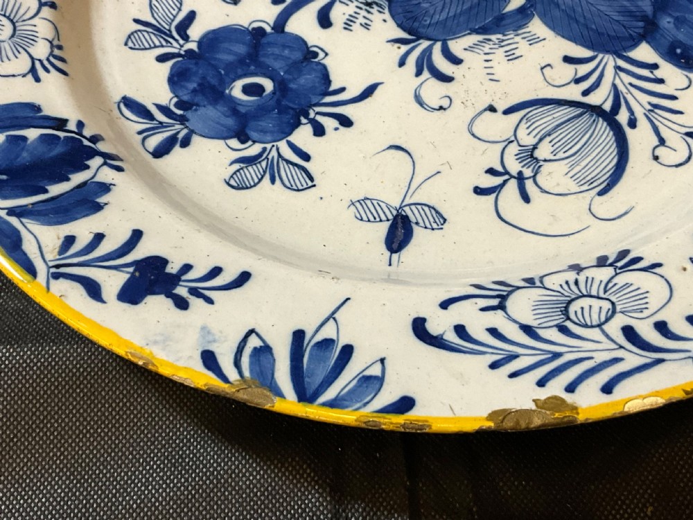 An antique circular tin-glazed earthenware plate featuring hand-painted cobalt blue floral motifs on a white background with a yellow rim. View VII