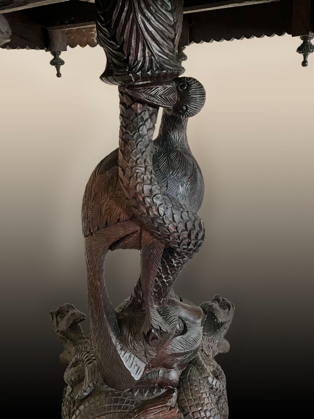 A 19th-century octagonal Burmese dark wood occasional table featuring detailed floral relief carvings, frieze drop finials, and a pedestal base carved as a mythical creature. View III