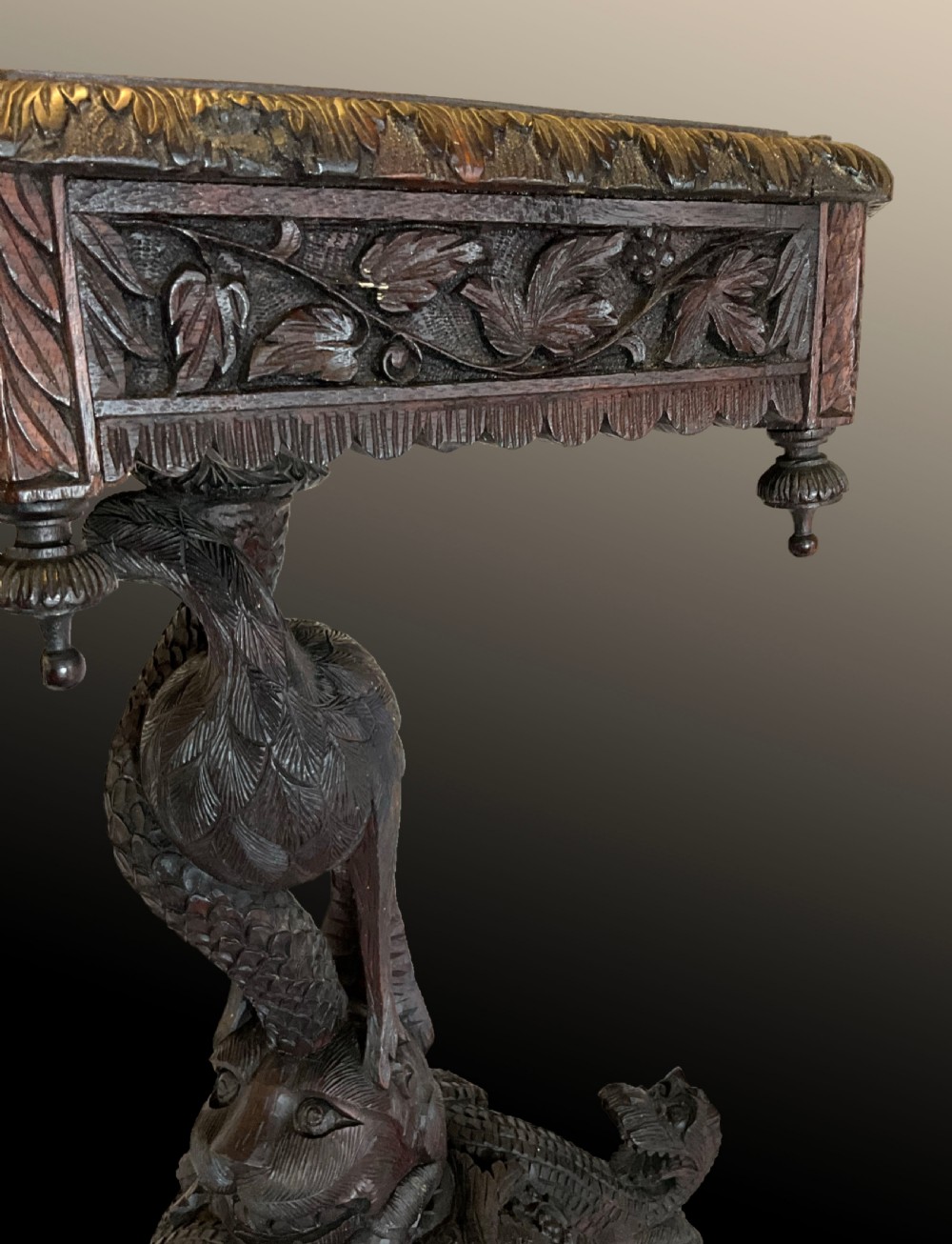 A 19th-century octagonal Burmese dark wood occasional table featuring detailed floral relief carvings, frieze drop finials, and a pedestal base carved as a mythical creature. View VI