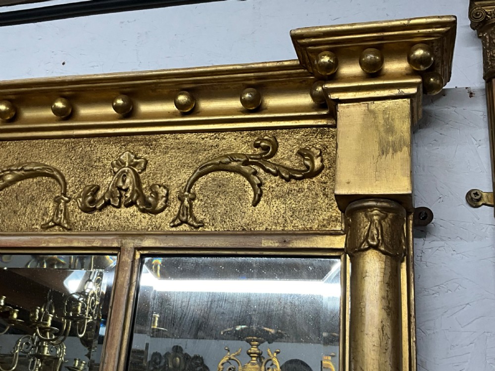 An early 19th-century Regency gilded overmantel mirror featuring a triple-plate mirror design, fluted columns, and ball moulding details. View II
