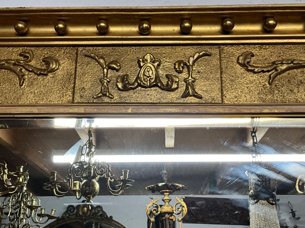 An early 19th-century Regency gilded overmantel mirror featuring a triple-plate mirror design, fluted columns, and ball moulding details. View IV