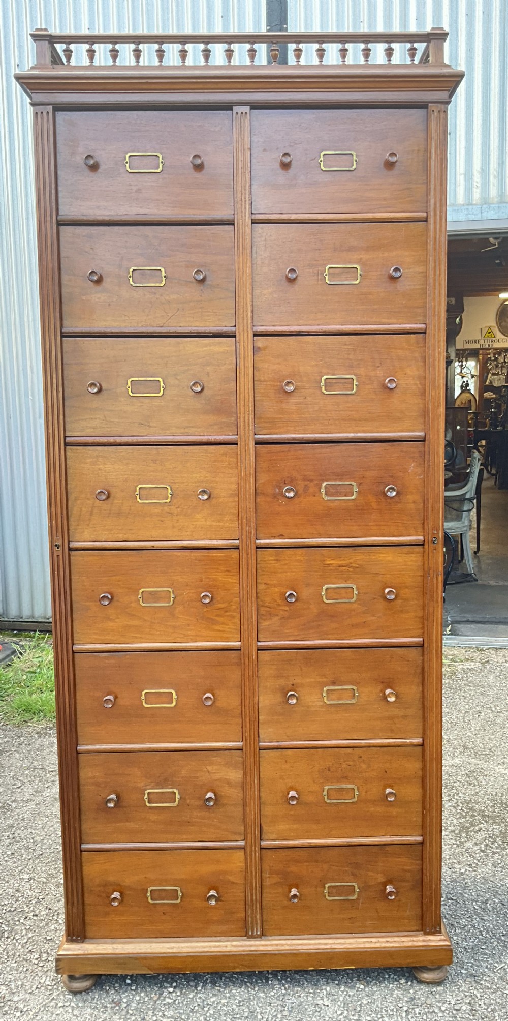 A tall 19th-century walnut bank of sixteen drawers featuring central brass label holders, turned wooden knobs, and a spindle gallery top rail.