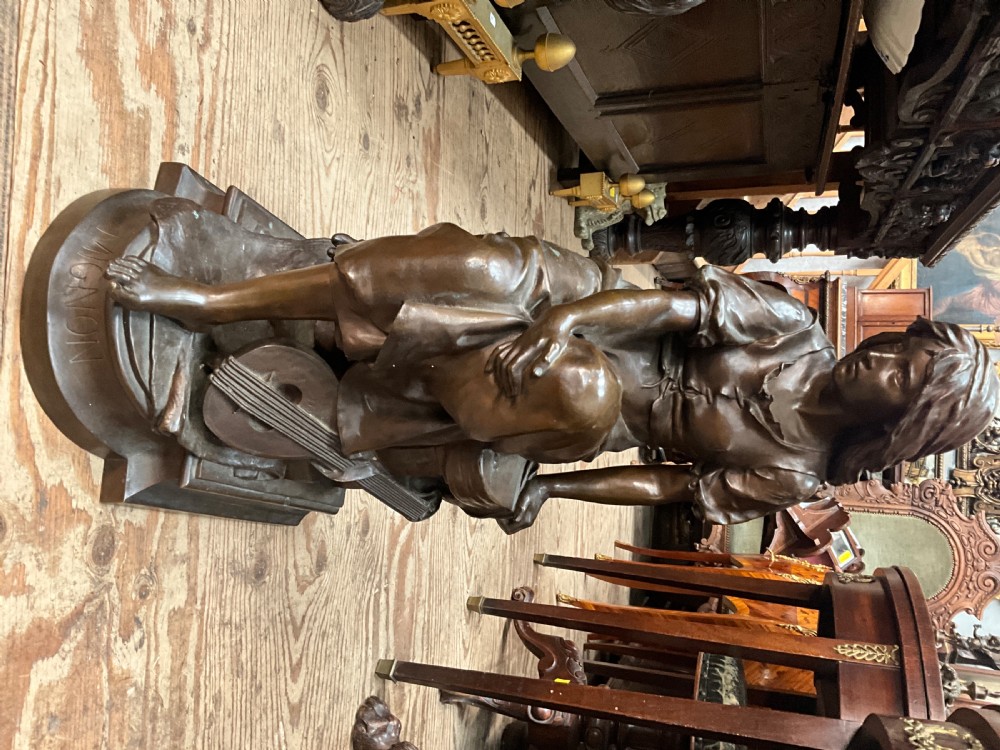 A dark patinated bronze statue depicting a seated young woman resting her foot on a rock next to a lute, with Mignon inscribed on the base. View II