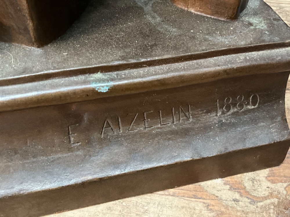 A dark patinated bronze statue depicting a seated young woman resting her foot on a rock next to a lute, with Mignon inscribed on the base. View IV