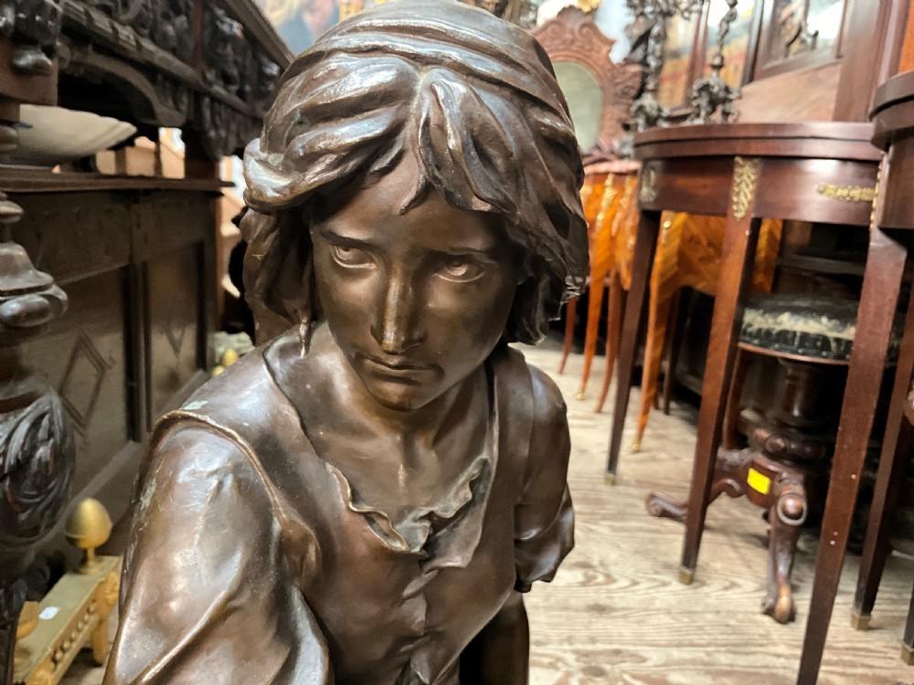 A dark patinated bronze statue depicting a seated young woman resting her foot on a rock next to a lute, with Mignon inscribed on the base. View IX