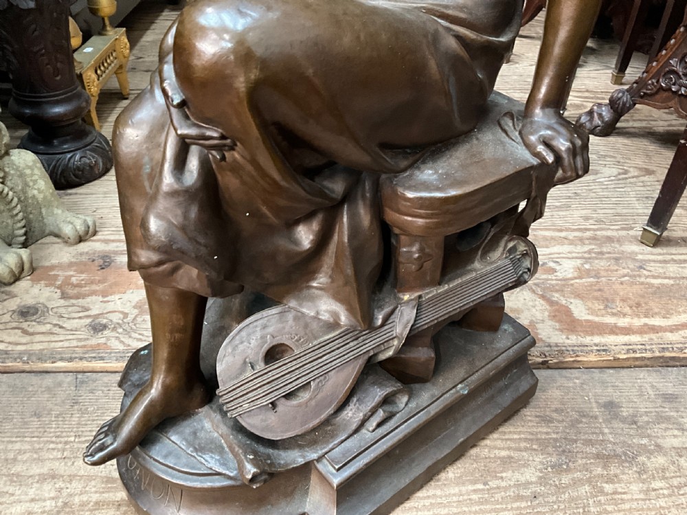 A dark patinated bronze statue depicting a seated young woman resting her foot on a rock next to a lute, with Mignon inscribed on the base. View XII