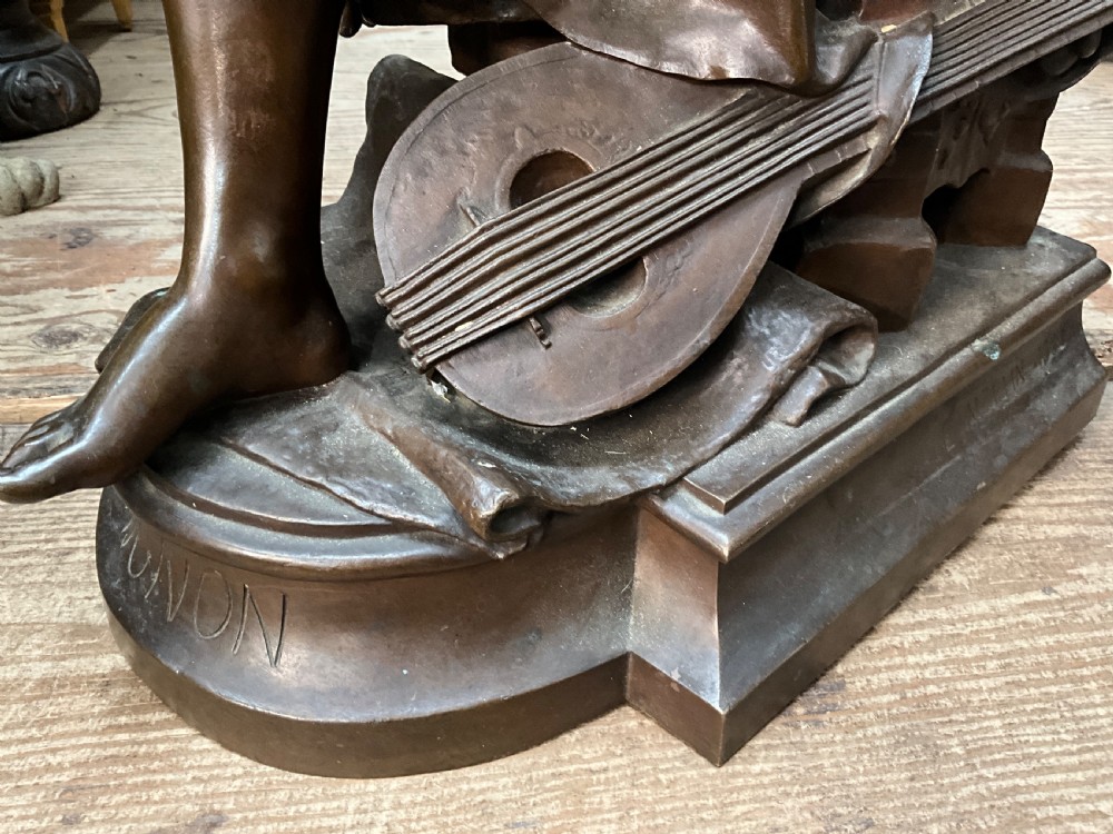 A dark patinated bronze statue depicting a seated young woman resting her foot on a rock next to a lute, with Mignon inscribed on the base. View XIII