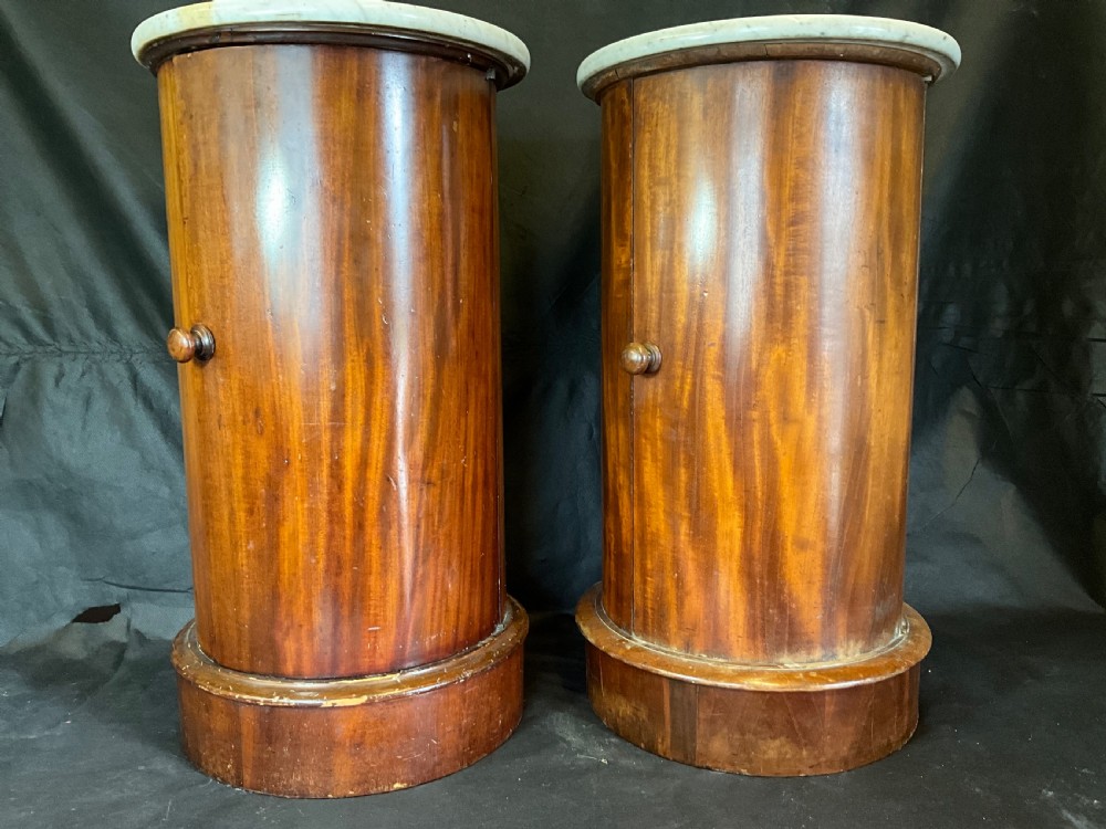 A matched pair of 19th-century Victorian cylindrical mahogany bedside cabinets featuring circular light grey marble tops, single curved doors with turned wooden knobs, and molded plinth bases.