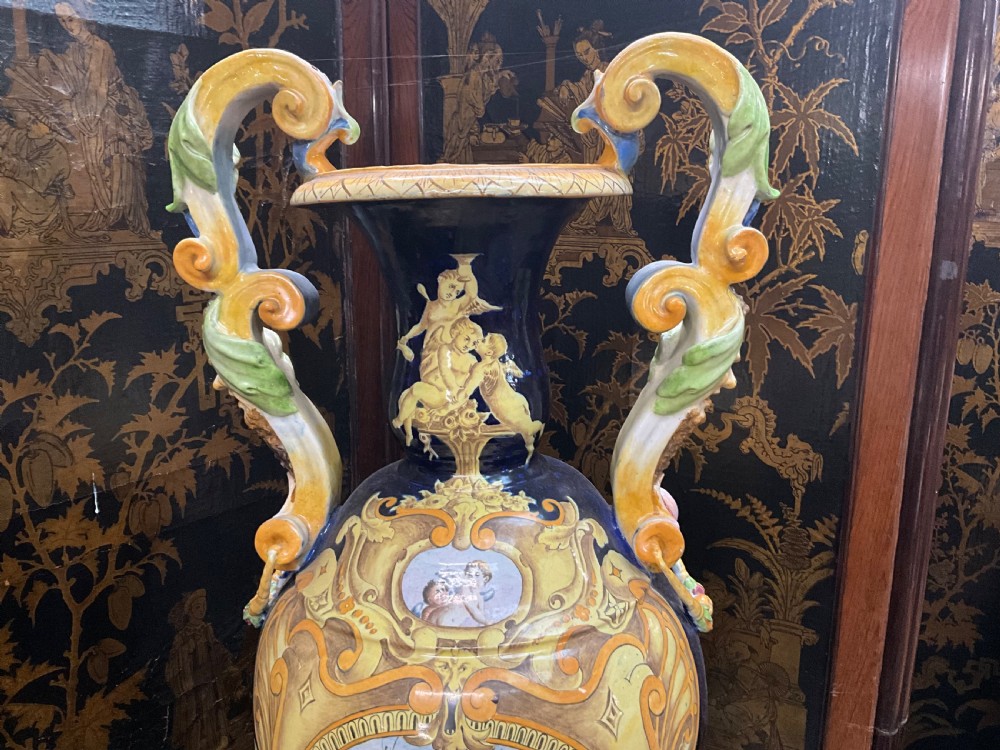 Large Italian Majolica tin-glazed earthenware vase with scrolled handles resting on an ornate matching pedestal base, decorated with painted mythological figures and relief masks. View II