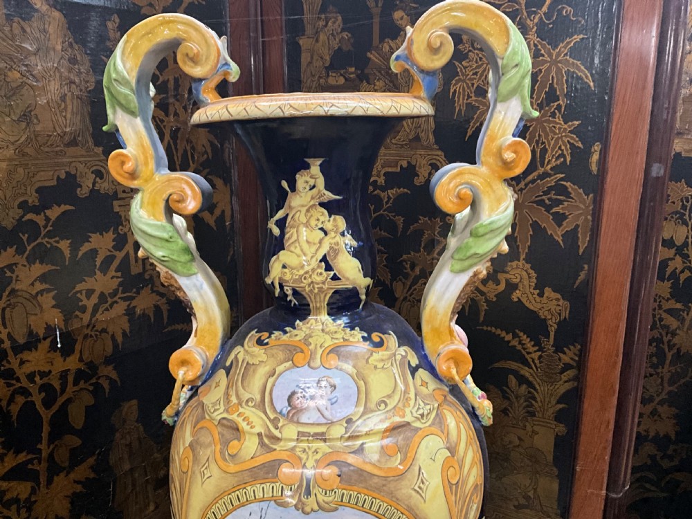 Large Italian Majolica tin-glazed earthenware vase with scrolled handles resting on an ornate matching pedestal base, decorated with painted mythological figures and relief masks. View III