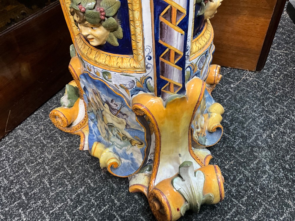Large Italian Majolica tin-glazed earthenware vase with scrolled handles resting on an ornate matching pedestal base, decorated with painted mythological figures and relief masks. View V