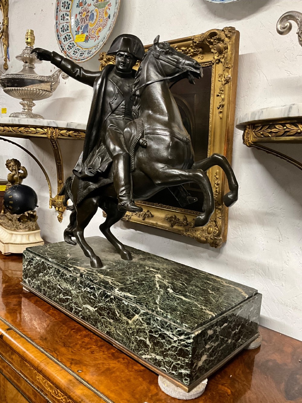 A dark bronze sculpture depicting Napoleon Bonaparte mounted on a rearing horse, set on a rectangular green marble plinth.