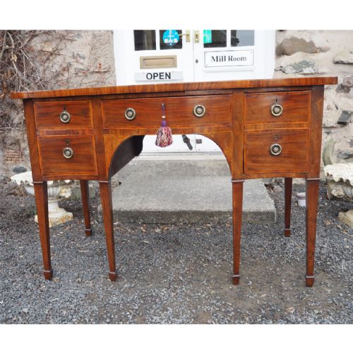 fig 1. A Georgian mahogany serpentine sideboard featuring a contoured front, five drawers with brass ring handles, and square tapered legs.