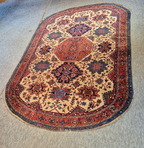 An antique hand-knotted Persian Bijar rug featuring a central terracotta medallion, geometric blue and red star motifs, a cream ground, and rounded curved ends. View II