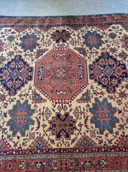 An antique hand-knotted Persian Bijar rug featuring a central terracotta medallion, geometric blue and red star motifs, a cream ground, and rounded curved ends. View IV