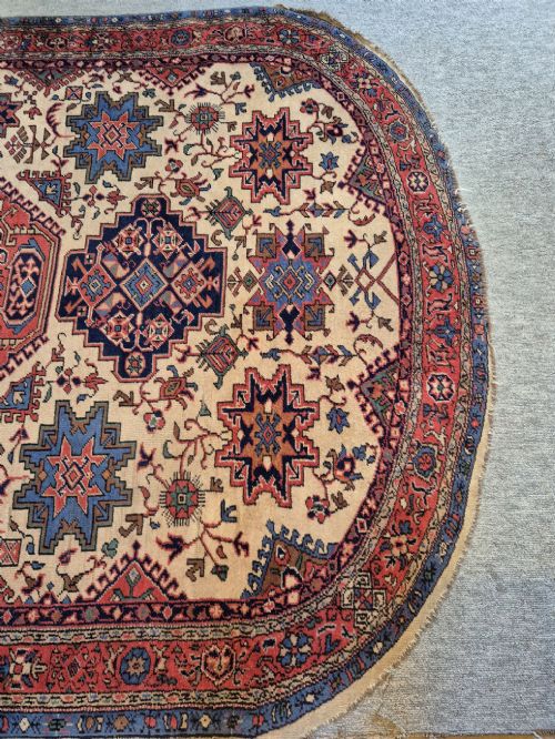 An antique hand-knotted Persian Bijar rug featuring a central terracotta medallion, geometric blue and red star motifs, a cream ground, and rounded curved ends. View V