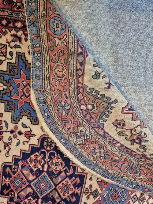 An antique hand-knotted Persian Bijar rug featuring a central terracotta medallion, geometric blue and red star motifs, a cream ground, and rounded curved ends. View VIII