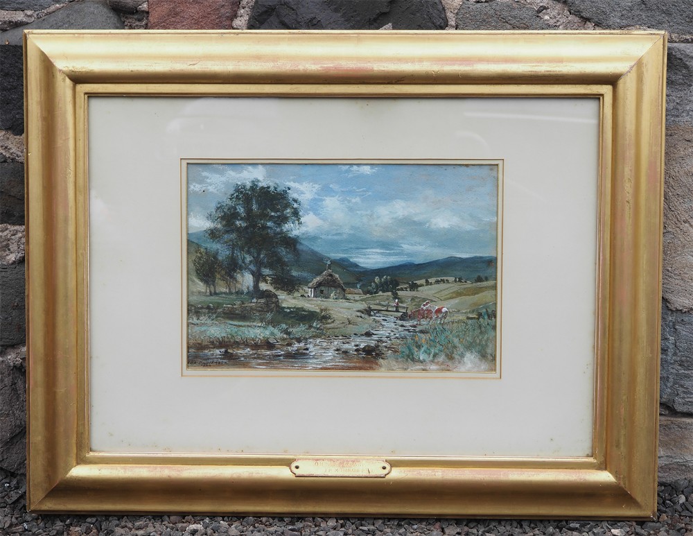 A framed Victorian landscape painting depicting a rural cottage beside a river set within a cream mount and wide gilded wooden frame.
