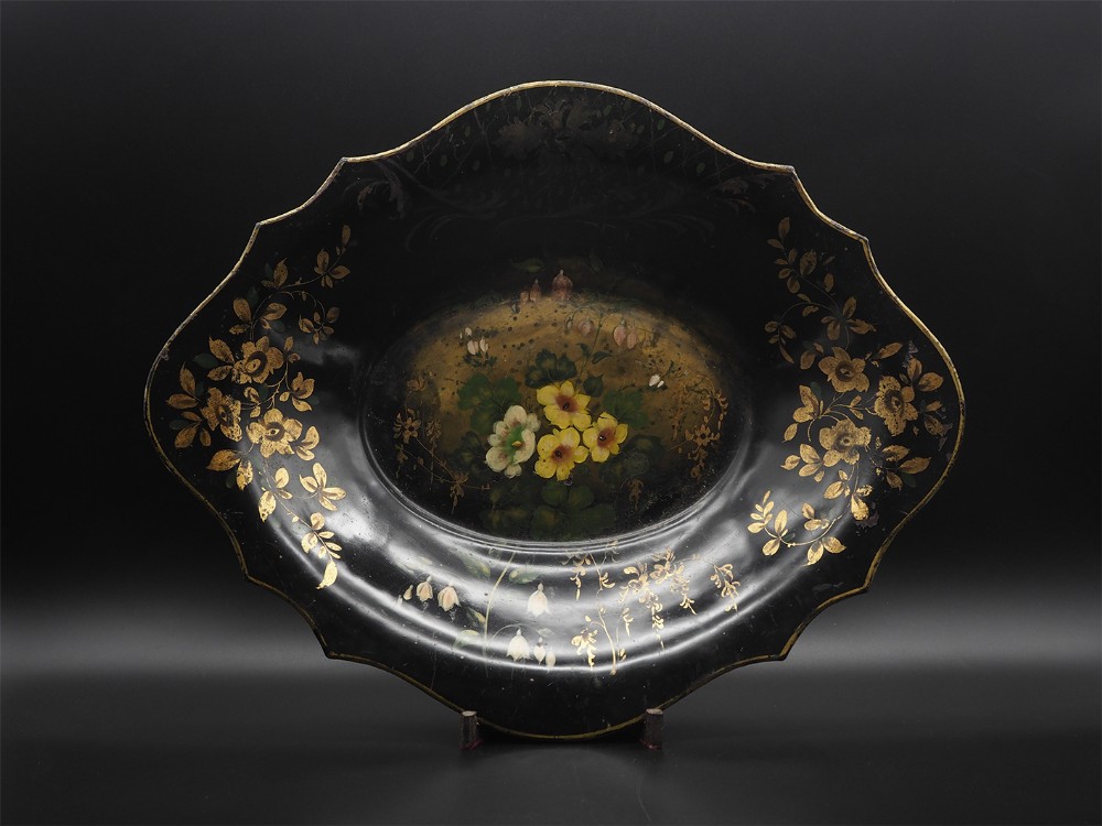 An early 19th-century oval black toleware bowl featuring a scalloped rim, hand-painted yellow floral centre, and gilded foliate border patterns.