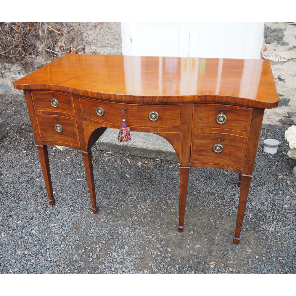 A Georgian mahogany serpentine sideboard featuring a contoured front, five drawers with brass ring handles, and square tapered legs.