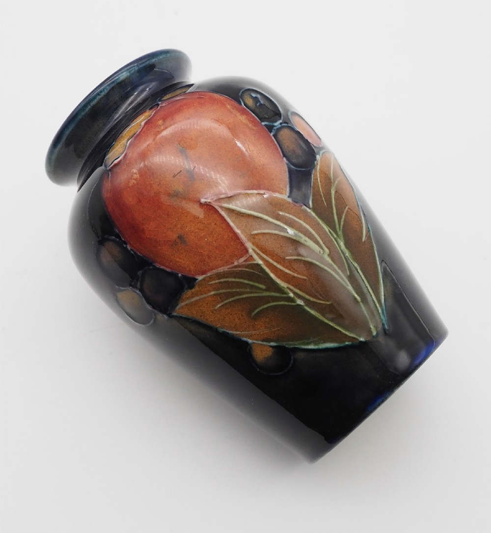 A small hand-painted Moorcroft miniature vase featuring tubelined pomegranate fruit and foliage over a dark cobalt blue ground.