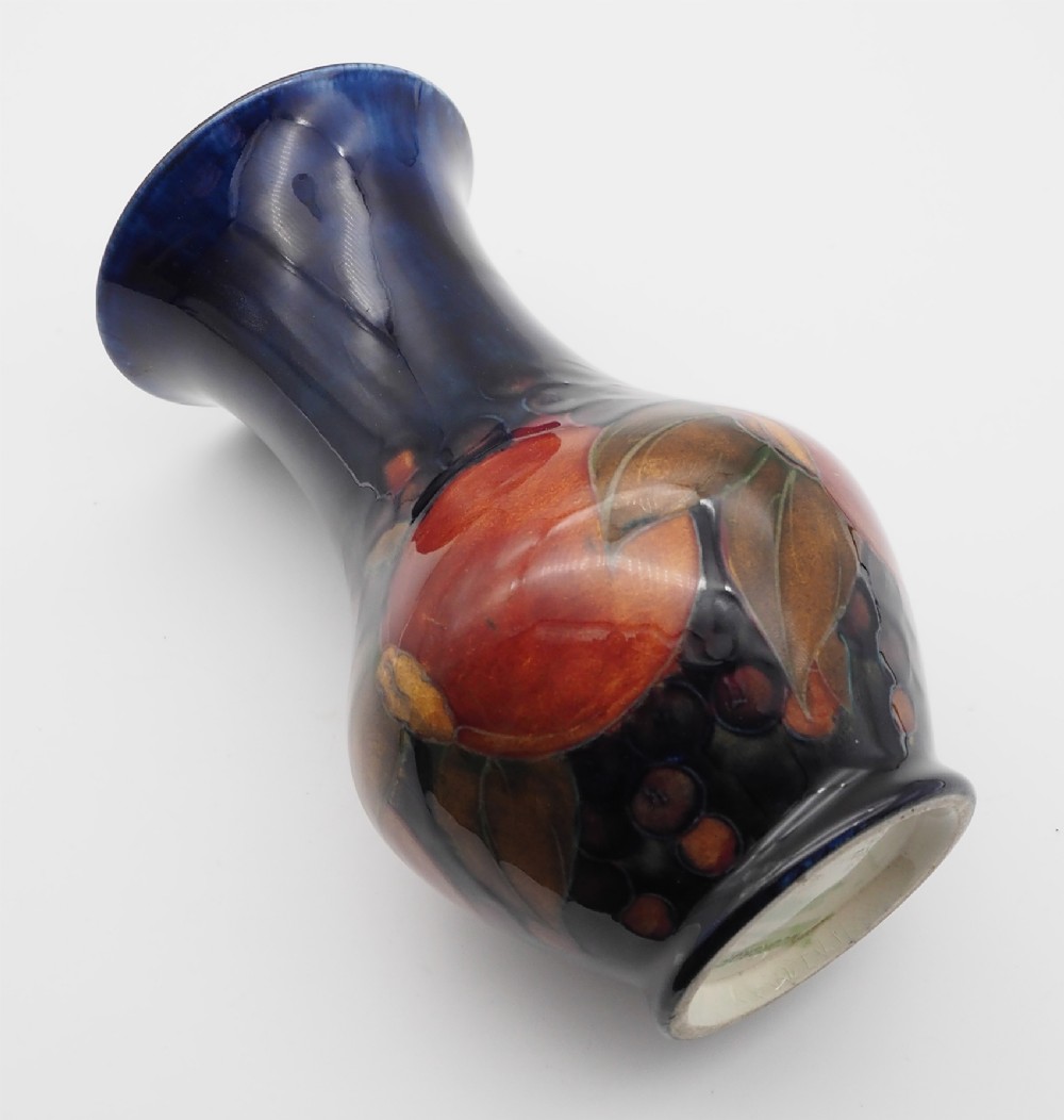 A William Moorcroft flared ceramic vase featuring hand-painted tube-lined pomegranates and dark berries against a deep cobalt blue glazed background.