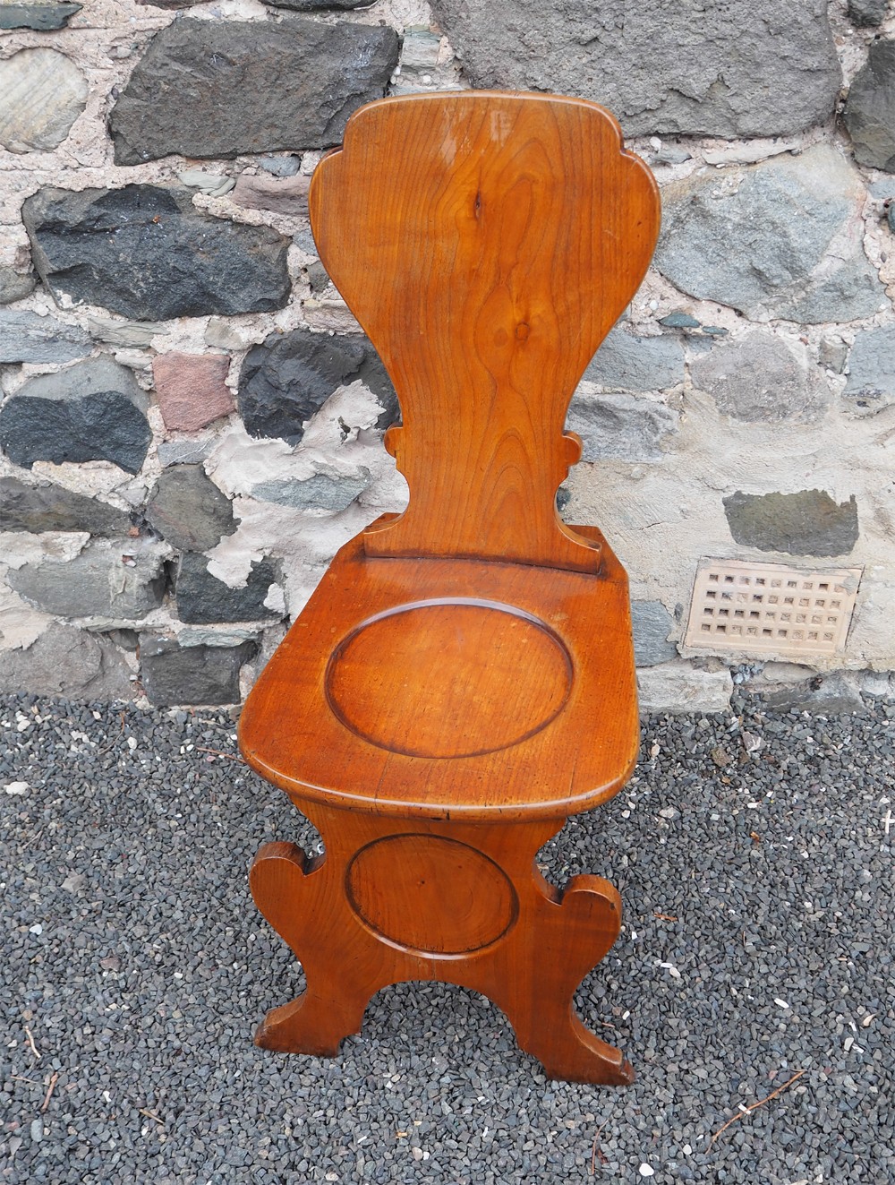 An eighteenth-century George II fruitwood sgabello hall chair with a shaped cartouche back, circular recessed seat, and carved slab trestle base.