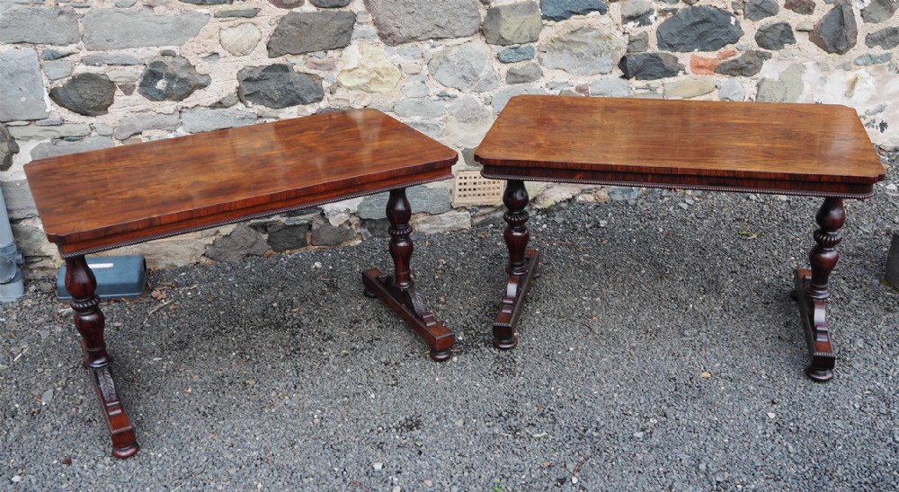 A matched pair of antique rosewood library tables featuring polished rectangular tops, beaded aprons, turned pedestal supports, and carved trestle bases.