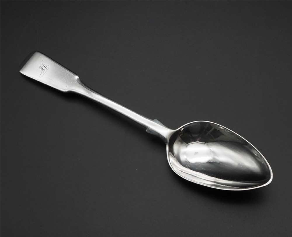 An antique silver spoon featuring a fiddle pattern handle with an engraved monogram and an oval bowl.