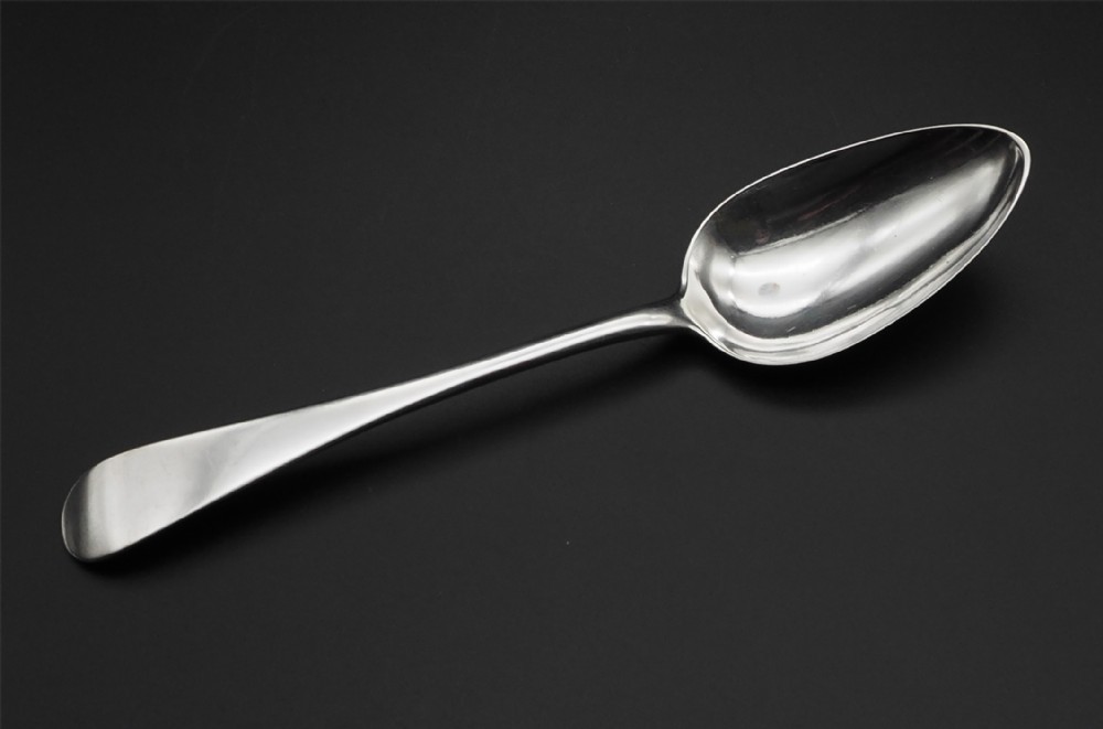 An antique Scottish silver table spoon with an oval bowl and a smooth, polished handle set against a dark background.