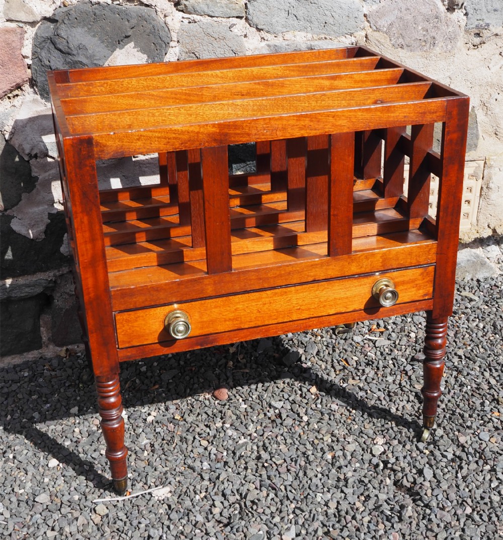 A dark brown mahogany Regency canterbury features slatted dividers, a single long drawer with two brass knobs, and turned legs on castors.