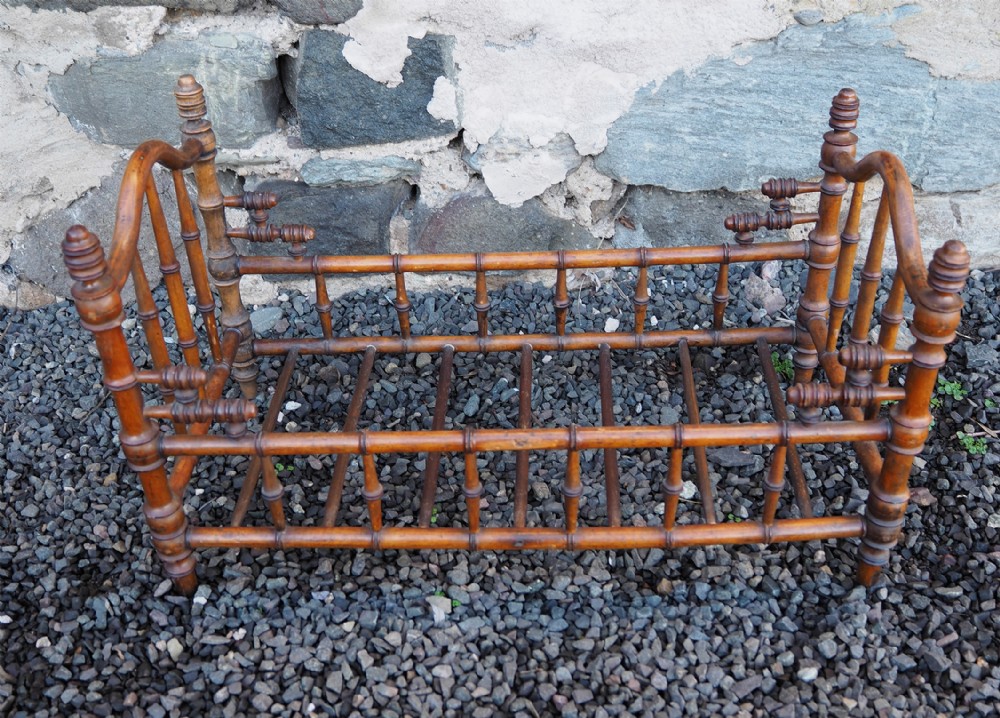 A small turned wood miniature dolls bed featuring spindle rails, finials, and a slatted base in a warm brown finish.