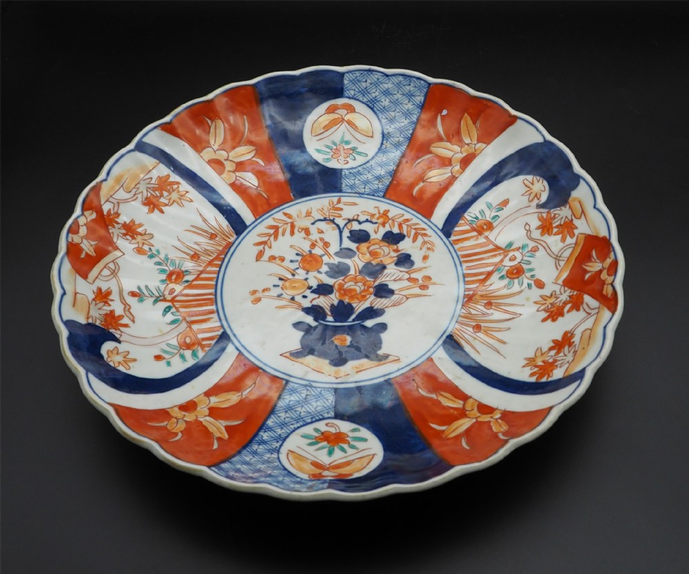 A circular 19th-century Japanese Imari porcelain charger with a scalloped edge, central floral basket motif, and radiating blue and iron-red panels.