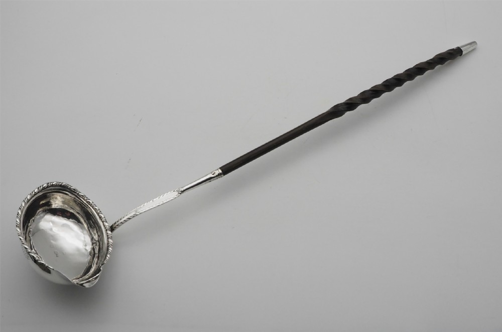 An eighteenth-century silver toddy ladle featuring an oval bowl with a pouring lip and a long dark twisted handle.
