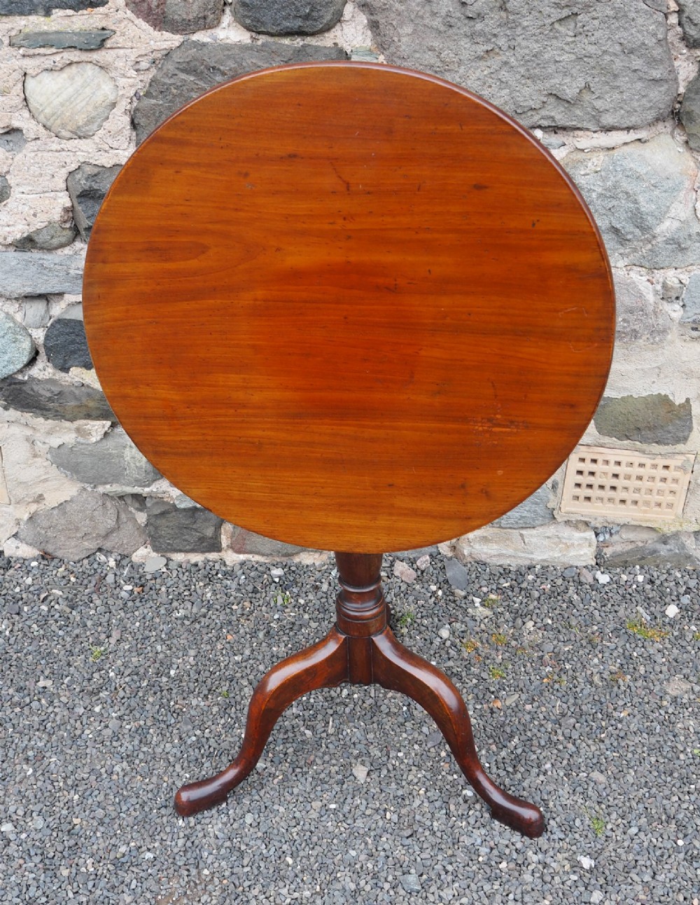 A Georgian mahogany tilt-top table shown upright with a circular top, turned central pedestal, and tripod cabriole legs.