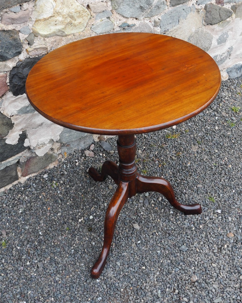 A Georgian mahogany tilt-top table shown upright with a circular top, turned central pedestal, and tripod cabriole legs. View II