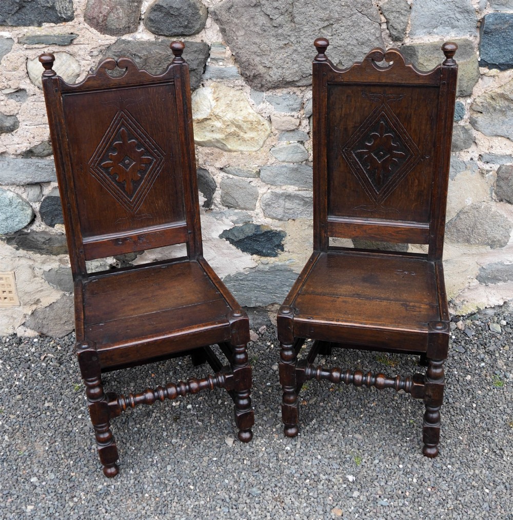 A pair of dark carved oak 17th-century hall chairs featuring geometric diamond back panels and turned legs.