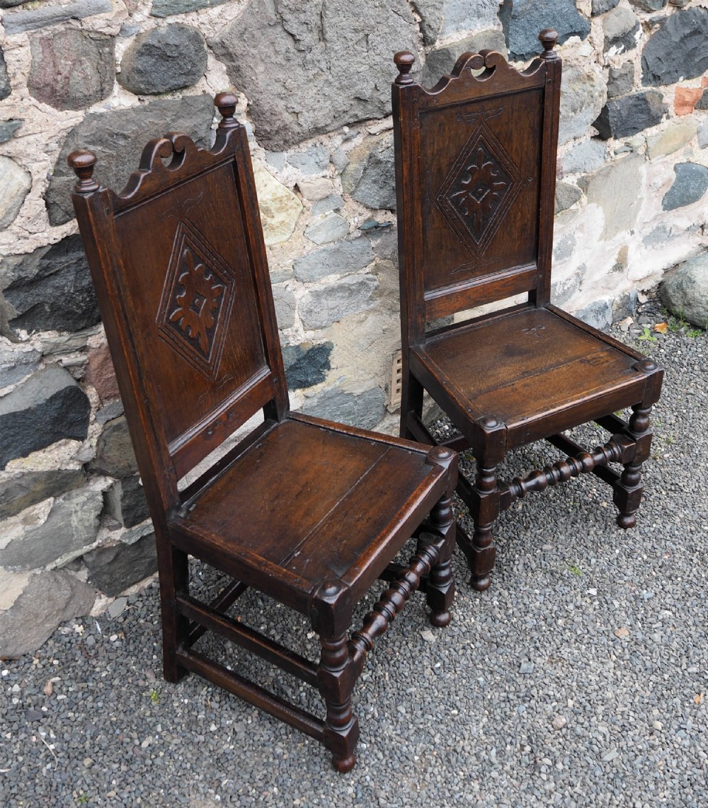 A pair of dark carved oak 17th-century hall chairs featuring geometric diamond back panels and turned legs. View II