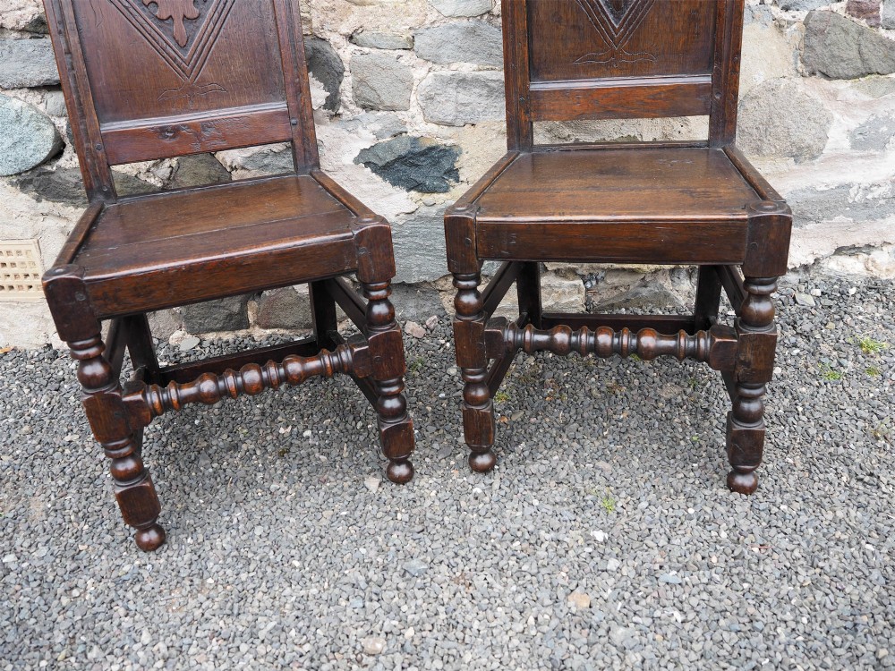 A pair of dark carved oak 17th-century hall chairs featuring geometric diamond back panels and turned legs. View III