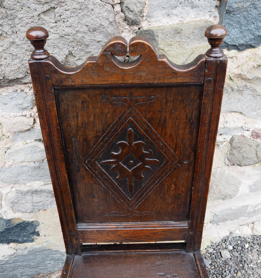 A pair of dark carved oak 17th-century hall chairs featuring geometric diamond back panels and turned legs. View V